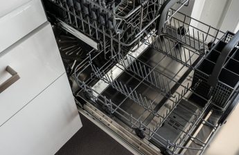 A clean and empty stainless steel dishwasher open in a modern kitchen setting.